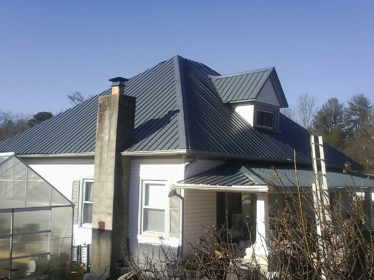 Dark blue standing seam metal roof on a white farmhouse with dormer — Slate & Tile Roof Repair by Roofing Brothers in Northport