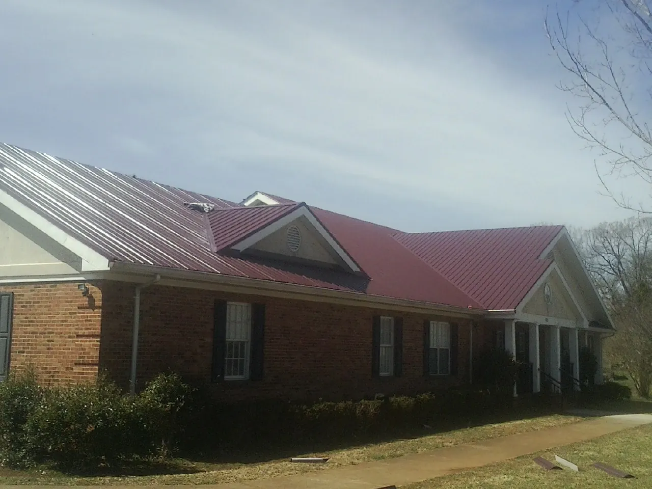 Red metal roof with gabled entries on a long brick building, from a Hail Damage Roof Repair job in Northport