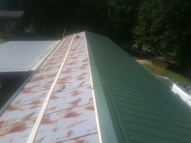 Old rusted panels beside newly installed green metal roofing — Wind Damage Roof Repair by Roofing Brothers in Northport