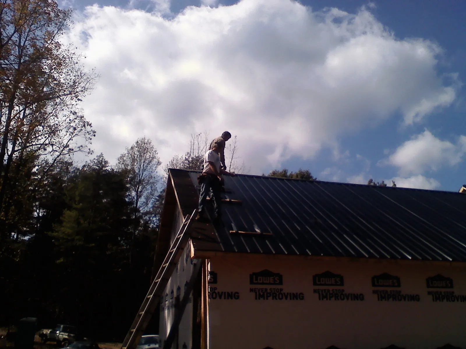 Roofer fastening dark metal panels high against a cloudy sky, from a Roof Inspection job in Northport